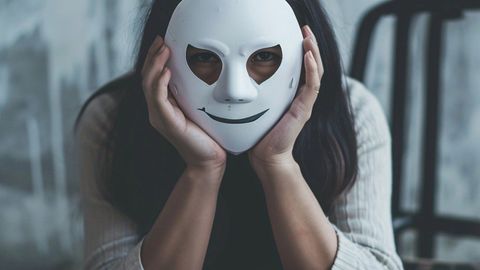 顔の前に白い仮面を持つ若い女性