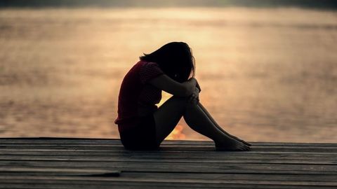 Une personne assise seule au bord de l’eau au crépuscule