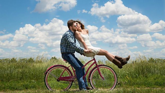 野原で自転車に乗りながらキスをするカップル