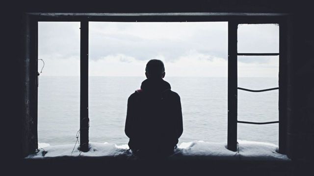 大きな窓の前に一人で立つ人のシルエット