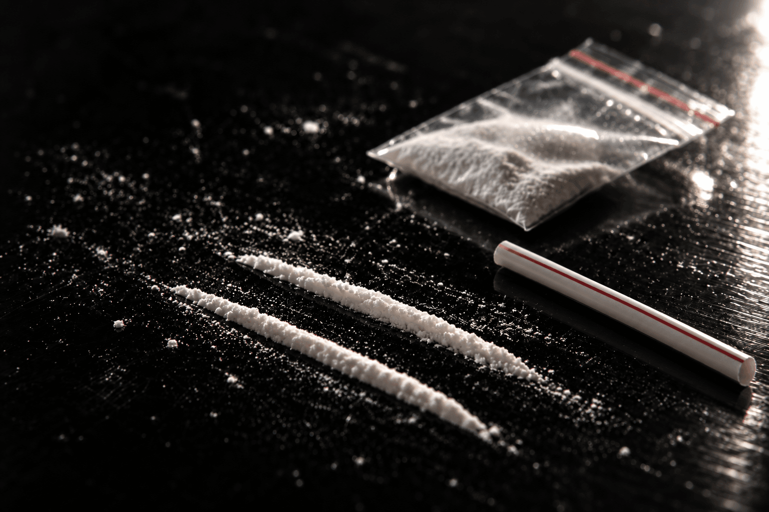 Deux lignes de cocaïne, un sachet de poudre blanche et une paille sur une table noire