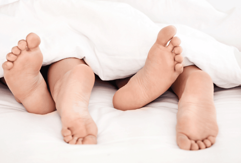 Dos personas tumbadas bajo un edredón con los pies visibles