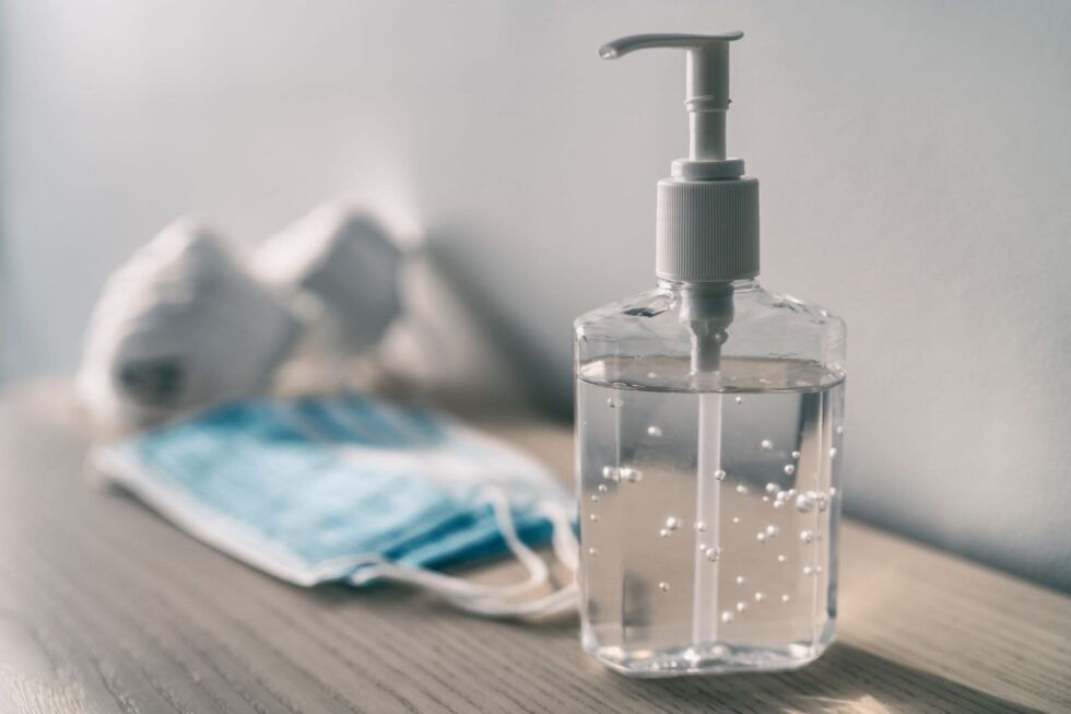 Frasco de gel hidroalcohólico con una mascarilla al fondo