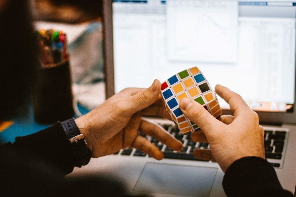 Una persona manipula un cubo de Rubik delante de un ordenador